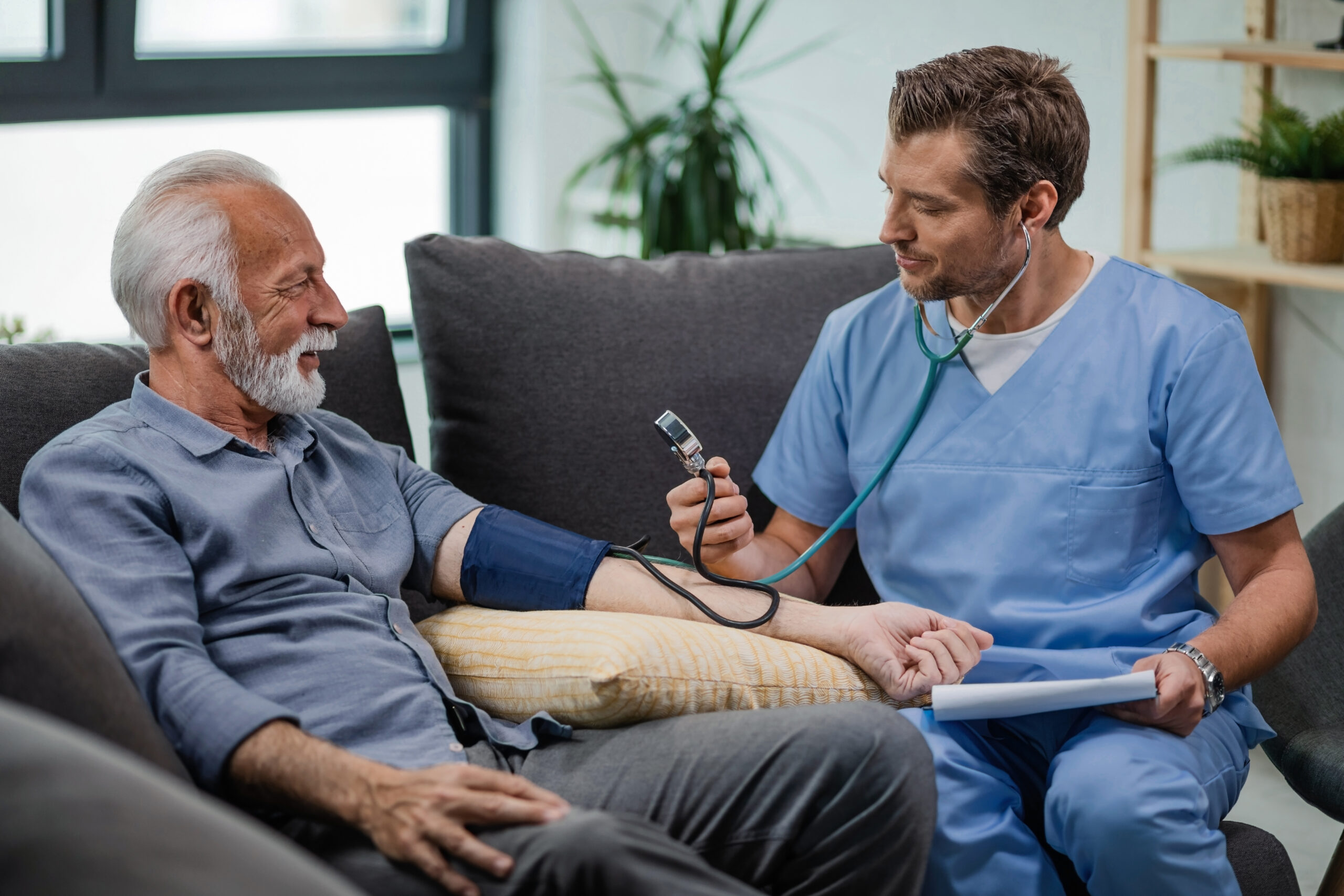 Happy general practitioner measuring blood pressure of mature man while being in a home visit.