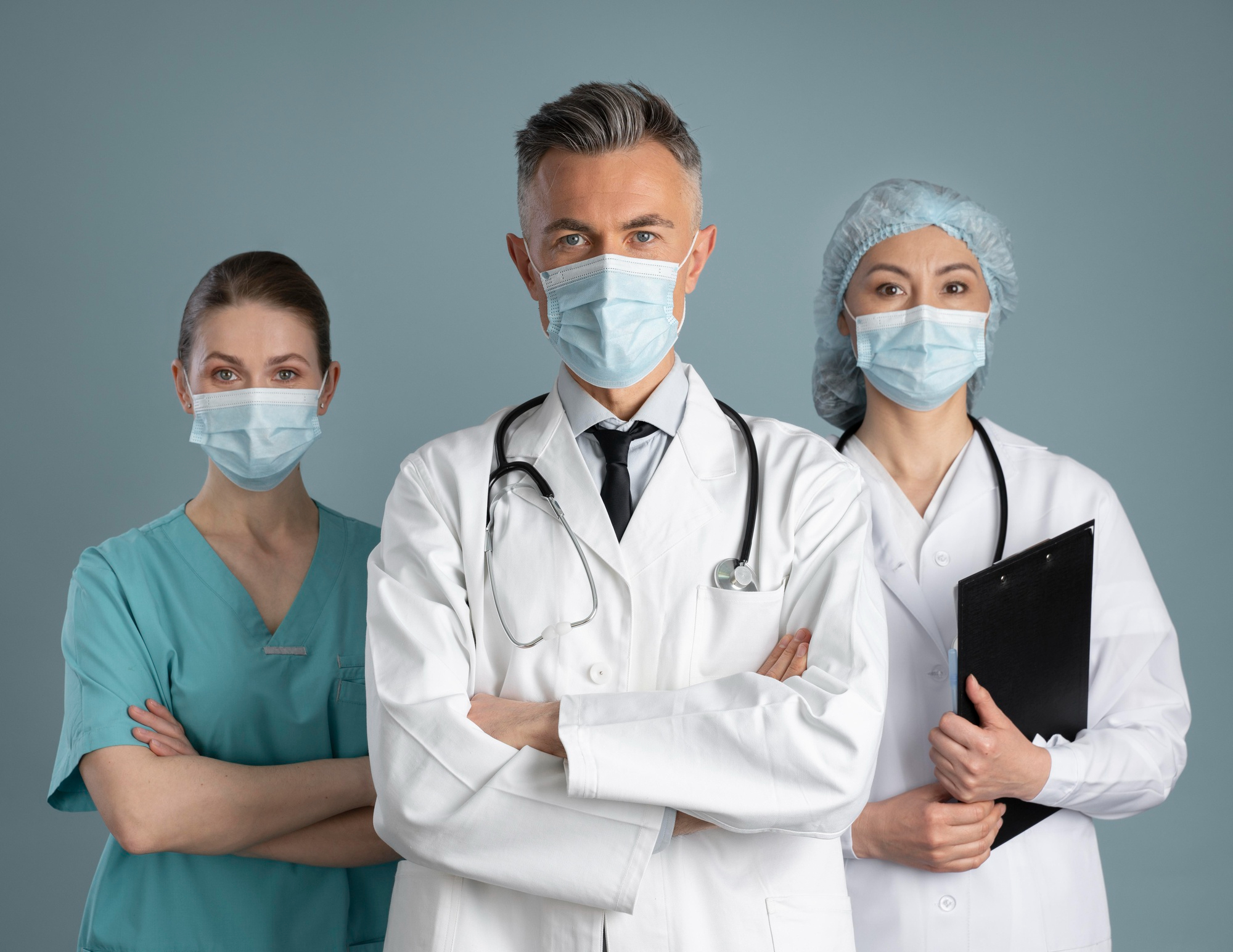 Medical team of three healthcare professionals wearing face masks, including a doctor with a stethoscope and two nurses, standing confidently.
